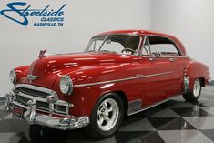 an old red car sitting on top of a black and white checkered floor