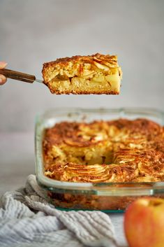 a person holding a piece of apple pie over a casserole in a glass dish