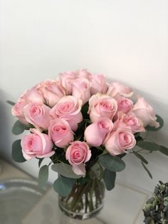 a glass vase filled with pink roses on top of a marble table next to a plant