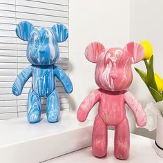 two colorful teddy bears sitting next to each other on a counter with flowers in vases