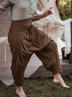 a woman standing in the grass with her hands on her hips and wearing brown pants