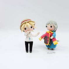 two miniature knitted dolls standing next to each other on a white surface with one holding the hand of another doll