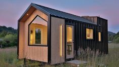 the tiny house is lit up at night in the field with tall grass and trees