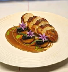 a white plate topped with meat covered in sauce and flower garnishments on top of it