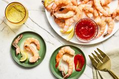 two plates with shrimp, lemon wedges and ketchup on them next to silverware