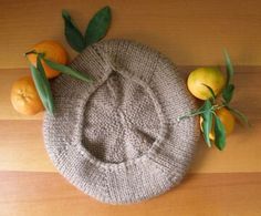 a knitted hat sitting on top of a wooden table next to oranges and leaves