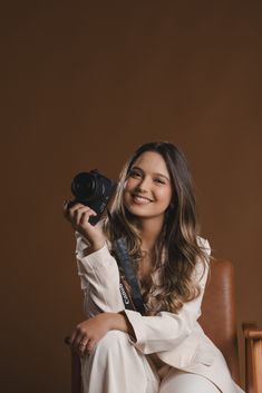 a woman sitting in a chair holding a camera up to her face and smiling at the camera