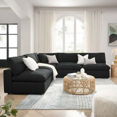 a living room filled with black couches and white pillows on top of a rug