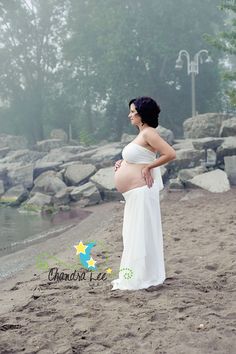 a pregnant woman is standing on the beach with her belly wrapped in a white dress