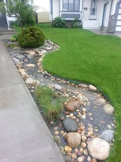 a house with grass and rocks in the front yard, next to a walkway that leads up to it