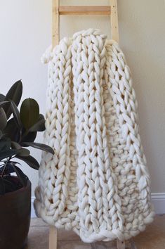 a white blanket sitting on top of a wooden ladder next to a potted plant