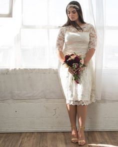 a woman is standing in front of a window with her hands on her hips and holding a bouquet of flowers