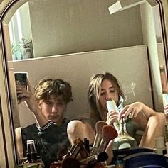 a man and woman sitting in front of a mirror taking pictures with their cell phones