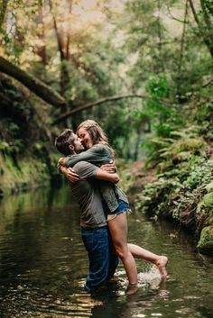 a man and woman hug in the water while standing next to each other on a riverbank