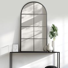 a mirror sitting on top of a table next to a vase with a plant in it