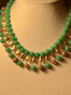 Lovely and lavivish jade-green bead and gold tone fringe necklace. Green swirled 10mm jade colored beads  paired with textured gold tone beads and gold tone spacer beads. This necklace is a delight for fans of Cleopatra or the Egyptian Revival period. The fringe extends 1 inch from the necklace line and  is 17 inches long. Excellent shape with little wear. Not signed with a ring clasp. (H141) Green And Gold Beaded Necklace, Egyptian Beaded Jewelry, Gold Beaded Jade Necklace, Gold Jade Beaded Necklaces With Gemstone Beads, Gold Jade Beaded Necklaces With Gemstones, Gold Jade Gemstone Beaded Necklaces, Gold Jade Necklaces With Round Beads, Gold Jade Necklace With Gemstone Beads, Gold Jade Beaded Necklaces With Round Beads