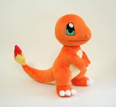 an orange stuffed animal with green eyes and white legs sitting on a white surface next to a small red object