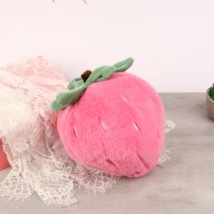 a pink stuffed strawberry sitting on top of a table next to a potted plant