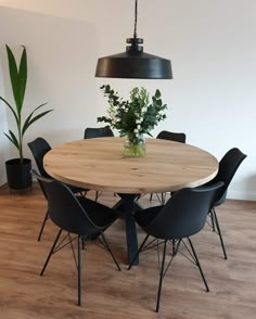 a round wooden table with black chairs and a plant in the center is surrounded by potted plants