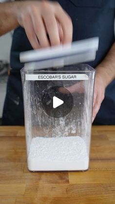 a person pouring sugar into a blender on top of a wooden table