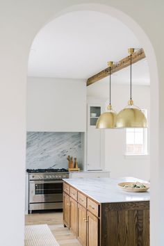 a kitchen with an archway leading to the dining room and living room, as well as two pendant lights hanging from the ceiling