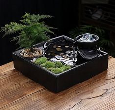 a bonsai tree in a black tray with rocks and stones on the bottom, sitting on a wooden table