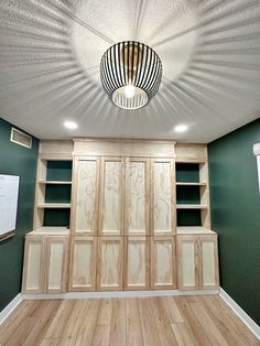 an empty room with green walls and wood flooring in the center is lit by a round light fixture