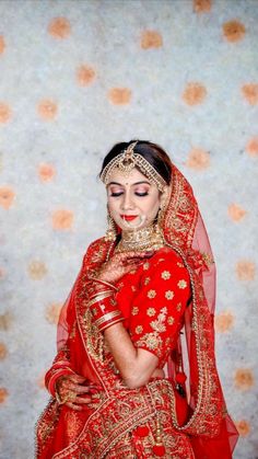 a woman in a red and gold bridal outfit posing for the camera with her hands on her chest