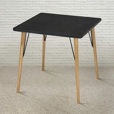 a black table with wooden legs against a white brick wall