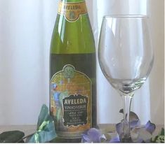 a bottle of wine next to a glass on a table with purple flowers and greenery