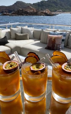 three glasses filled with drinks sitting on top of a table next to a couch and water