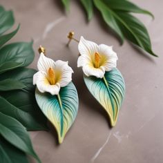 two white flowers with green leaves on a table next to each other and one yellow flower in the center