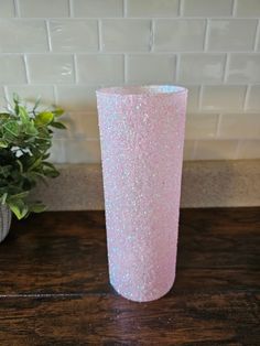 a pink vase sitting on top of a wooden table next to a potted plant