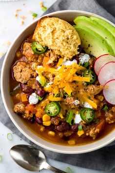 a white bowl filled with chili and cornbreads next to an avocado