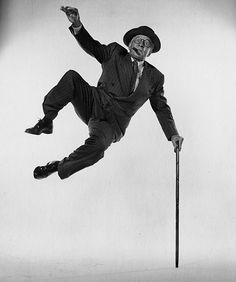 a man in a suit and hat is doing tricks on a pole with a cane