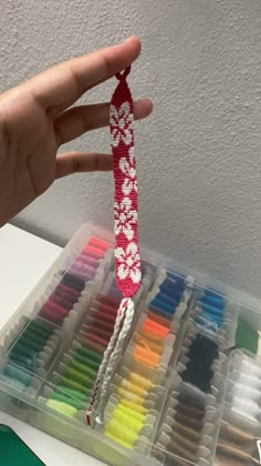 a hand holding a red string with white flowers on it in front of a box of colored crayons