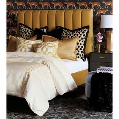 a bed with gold and black pillows on top of it next to a night stand