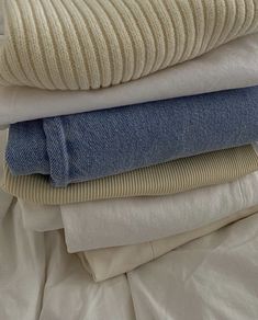 stack of folded clothes on bed with white sheets and blue jeans in foreground, closeup