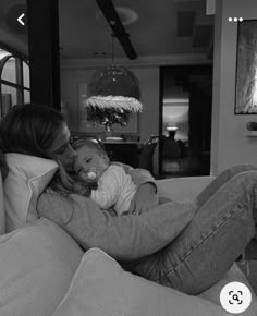 a woman sitting on a couch holding a baby in her lap and kissing her cheek