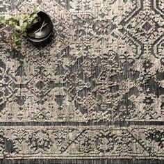 a black bowl sitting on top of a rug next to a vase with a plant in it