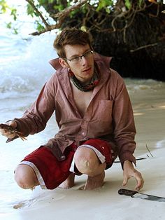 a man kneeling down on the beach with a fish in his hand and other items around him