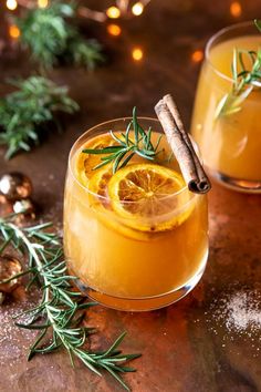 two glasses filled with orange juice and cinnamon stick garnished with rosemary on top