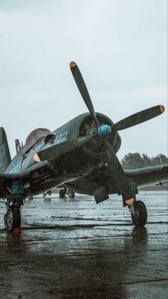 an old propeller plane sitting on top of a wet runway