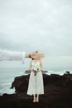 a woman in a white dress standing on top of a cliff next to the ocean