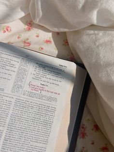 an open book laying on top of a bed covered in white sheets and blankets with pink flowers