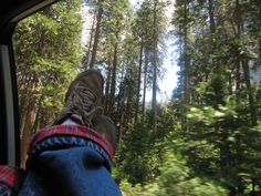 someone's feet hanging out the window of a car in front of some trees