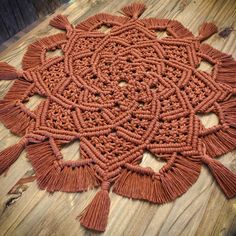 an orange doily with tassels on a wooden table next to a wood floor