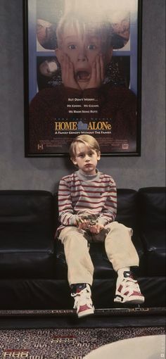 a young boy sitting on top of a black couch in front of a movie poster