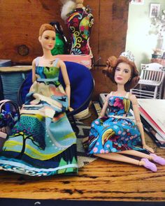 two dolls sitting on top of a wooden table next to a pile of books and other items