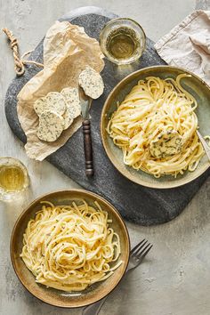 two bowls filled with pasta on top of a table next to wine glasses and crackers